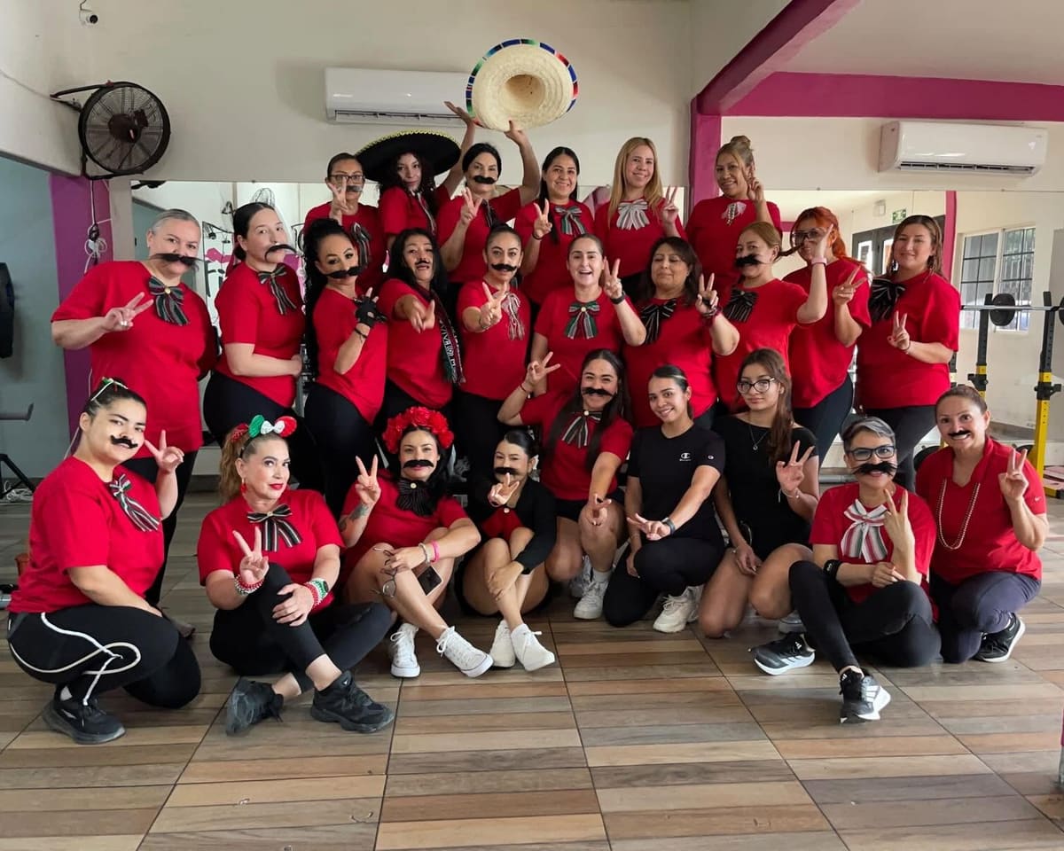 Alumnas de rojo con moño tricolor y bigote postizo, festejando las fiestas patrias en el gym
